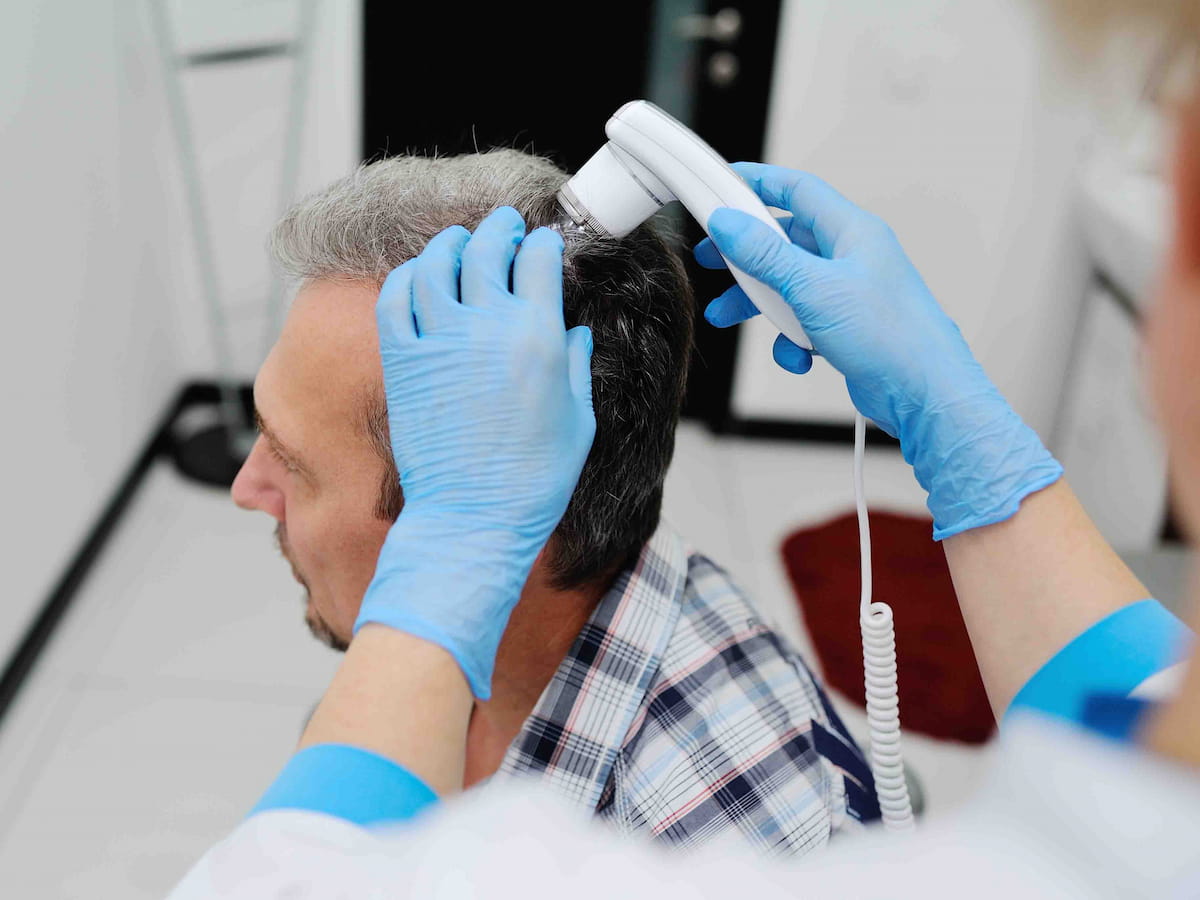 A man is inspecting hair and scalp with a diagnostic device in the clinic.
