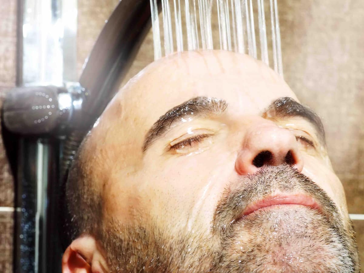 Man rinsing scalp under shower after recent hair transplant procedure