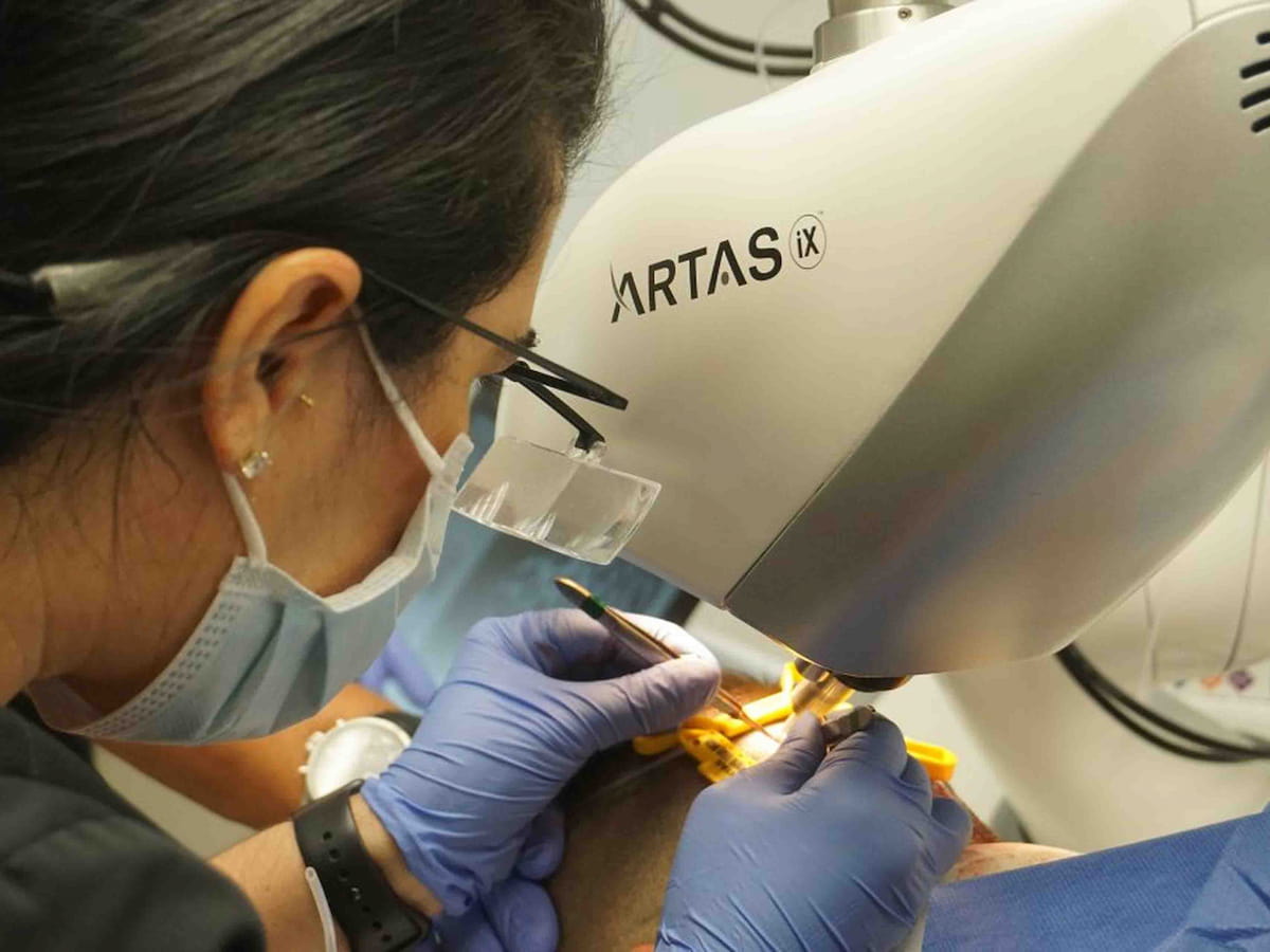 A doctor performing a robotic Artas hair transplant procedure using the Artas iX system.