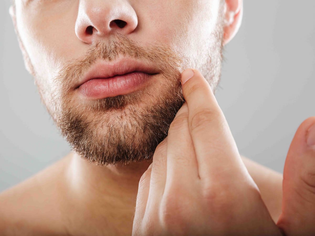 Close-up of a man touching his patchy beard, representing the concept of beard transplant and thinking what hair is used for beard transplant.
