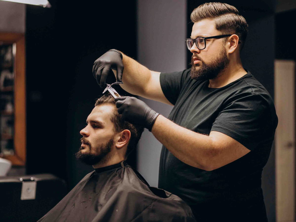 Barber carefully cutting a man’s hair with scissors, showing the safe method of how to cut hair after hair transplant.