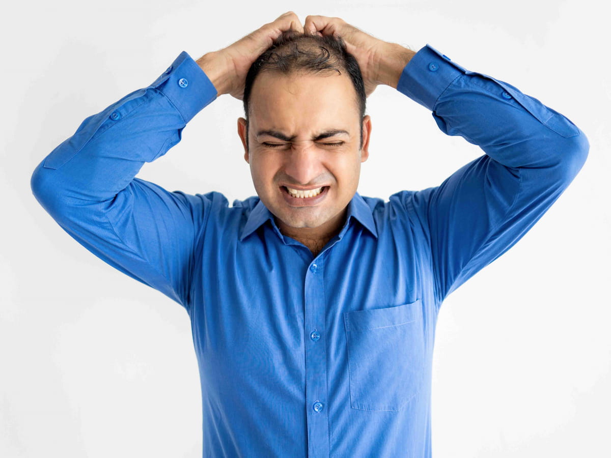 Man holding scalp and thinking how to deal with itching after hair transplant procedure.