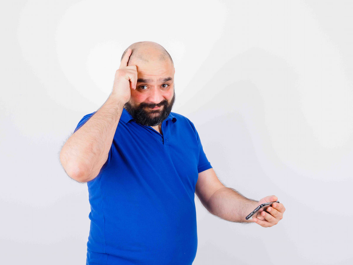A man touching the crown of his head while holding a phone, showing concern about crown hair grow after hair transplant.