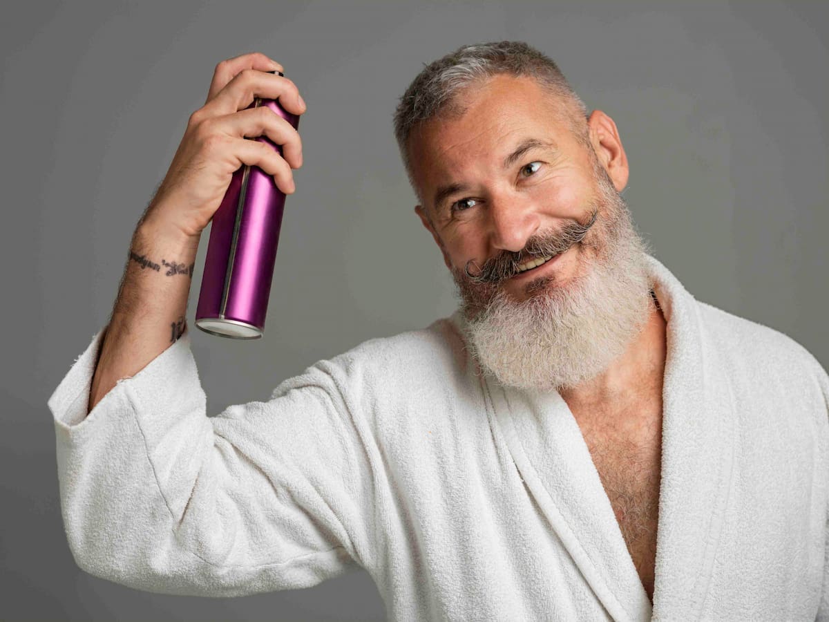 A smiling man applying hair styling product to his hair, representing when it is safe to use hair gel after hair transplant.