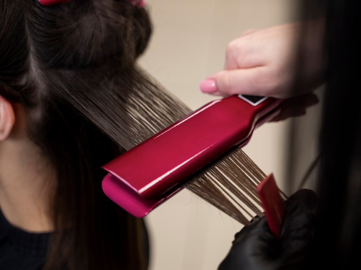 Close-up of a stylist using a flat iron to seal a keratin hair treatment on smooth brown hair in a salon.